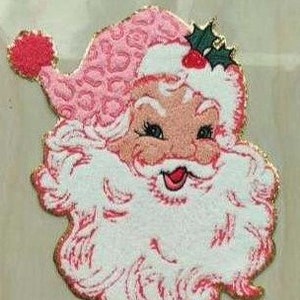 May include: A pink and white Santa Claus face with a smiling expression. The Santa hat has a leopard print design. The beard and hat trim are white with a gold glitter outline. A sprig of holly with red berries is on the hat.