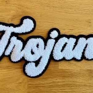 May include: White fluffy patch with the word "Trojans" in black outlined lettering.