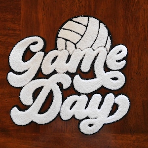 May include: White felt patch with black outlines that reads "Game Day" in a stylized font. A white volleyball is above the text.