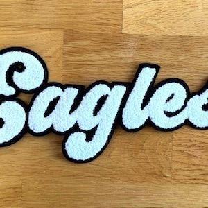 May include: White felt "Eagles" lettering with black outlines. The letters are in a cursive font.