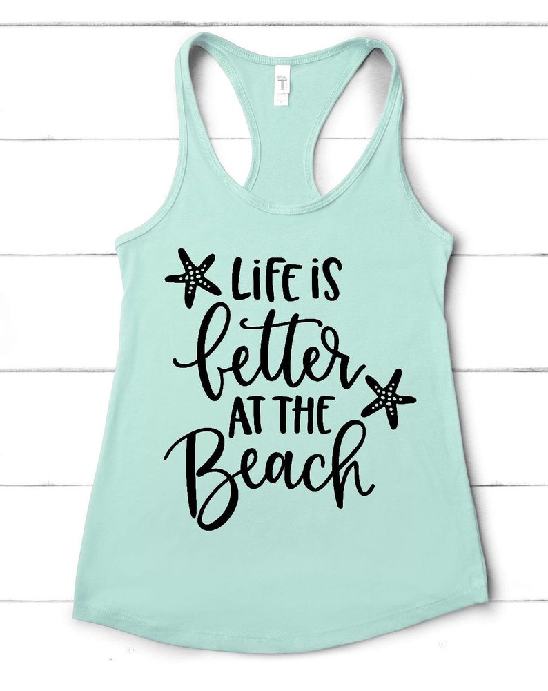 Pu&ograve; includere: Un top a spalline blu chiaro con il testo "Life is better at the beach" in corsivo nero con una stella marina nera su entrambi i lati del testo.