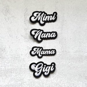 May include: Four black iron-on patches with white embroidered text. The patches read "Mimi", "Nana", "Mama", and "Gigi".