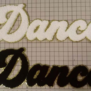 May include: Two felt patches with the word "Dance" in a cursive font. The top patch is white with gold trim and the bottom patch is black with gold trim.