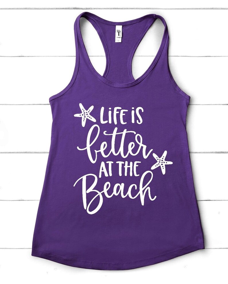 Pu&ograve; includere: Canotta viola con testo bianco che recita "Life is better at the beach" con una stella marina bianca su entrambi i lati del testo.