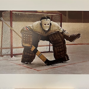 May include: A vintage print of a hockey goalie in a white mask and brown pads, crouched in front of a red net. The goalie holds a hockey stick with black and gold stripes. The image is set on an ice rink.