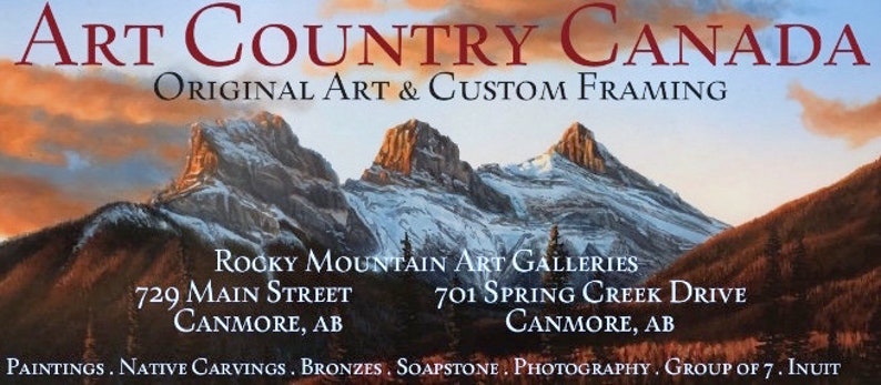 May include: A promotional image for Art Country Canada, featuring a mountain landscape painting. The text includes "Original Art & Custom Framing" and gallery addresses in Canmore, AB. Additional art forms listed include paintings, carvings, bronzes, soapstone, photography, and Inuit art.
