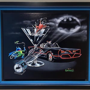 Puede incluir: Obra de arte enmarcada que representa un Batmóvil negro, una copa de Martini con salpicaduras y una figura de Batman. El fondo es negro con un símbolo de Batman y un foco. La obra está enmarcada en negro y azul.