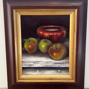 May include: Oil painting of a still life with a red bowl and three apples. The apples are green and red, and the bowl is a glossy red. The painting is in a dark brown frame with a gold inner border. Signed "Doris Rubin".