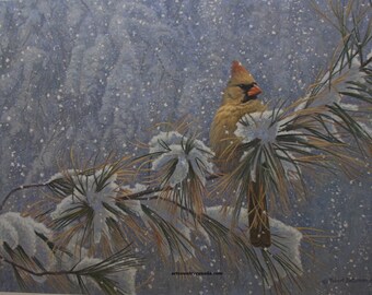 May include: A painting of a female cardinal perched on a snow-covered pine branch. The bird has a tan body, a red beak, and a small crest. The background is a snowy, blue-gray landscape with falling snowflakes. The artwork is signed by the artist.