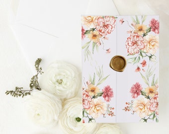 Op de afbeelding: Een bloemenuitnodigingsset met een witte envelop, een uitnodigingskaart met aquarelbloemen en een gouden zegel. Witte ranunculus bloemen en een klein decoratief bordje maken de opstelling compleet.