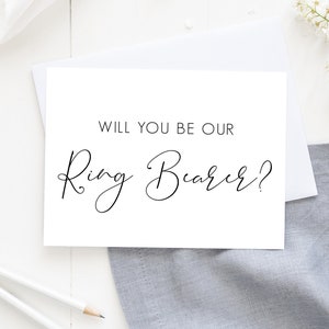 May include: White card with black calligraphy that reads "Will you be our Ring Bearer?"