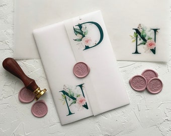 Puede incluir: Tres sobres blancos con un diseño floral y las letras D, N y N. Los sobres están sobre una superficie blanca texturizada con sellos de cera rosa.