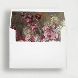 以下が含まれることがあります： 開いたフラップから詳細な花の絵が描かれた内側のライナーが見える白い封筒。このアートワークは、暗く質感のある茶色がかった灰色の背景に対して、濃いバーガンディ、ソフトピンク、白の花の房を表示しています。
