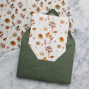 May include: A green envelope with a white floral patterned paper insert. The paper has a delicate design of small brown flowers and leaves.