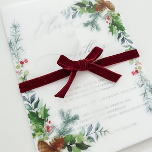 Side view of 5x7 vellum jacket for wedding invites with evergreen designs on the corner. Jacket is wrapped around a 5x7 invitation and meets in the middle. Red velvet ribbon is wrapped around and tied in a bow. Vellum wedding wrap to dress up card.