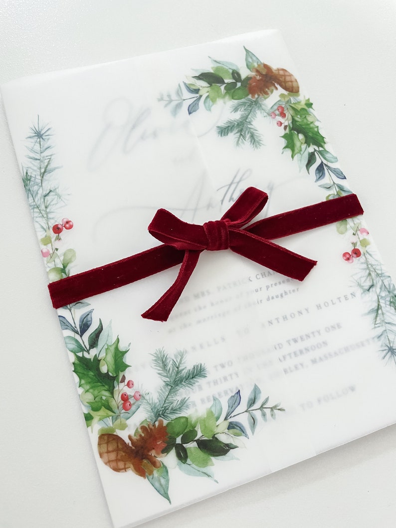 Side view of 5x7 vellum jacket for wedding invites with evergreen designs on the corner. Jacket is wrapped around a 5x7 invitation and meets in the middle. Red velvet ribbon is wrapped around and tied in a bow. Vellum wedding wrap to dress up card.