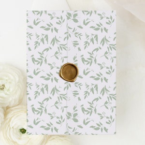 May include: A white envelope with a green leafy pattern and a gold wax seal. The envelope is perfect for a wedding invitation or other special occasion.