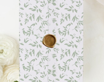 Puede incluir: Un sobre blanco con un patrón de hojas verdes y un sello de cera dorado. El sobre es perfecto para una invitación de boda u otra ocasión especial.