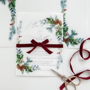 Christmas evergreen 5x7 vellum invite jacket with greenery and pine cone designs on the corner. Clear vellum wrap is wrapped around a 5x7 wedding invitation and meets in the middle.