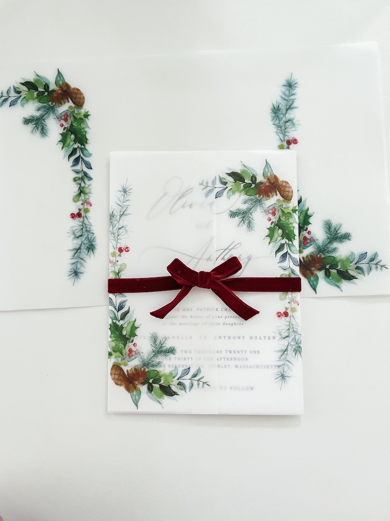 5x7 Christmas vellum jacket with wreath and evergreen designs on the corners. Vellum jacket is wrapped around a 5x7 invite and meets in the middle. Shown folded and flat.