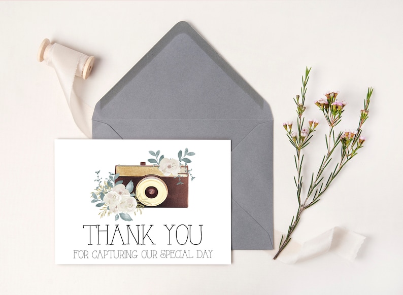 May include: A white thank you card with a vintage camera illustration surrounded by white flowers and green leaves. The text on the card reads "Thank You for Capturing Our Special Day."