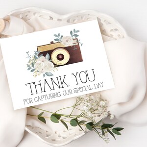 May include: A white thank you card with a vintage camera illustration and floral accents. The text reads "Thank You for capturing our special day."