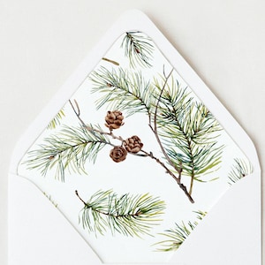 May include: White envelope with a pine branch and pine cone pattern on the flap. The pattern is a watercolor illustration of pine branches with brown pine cones.
