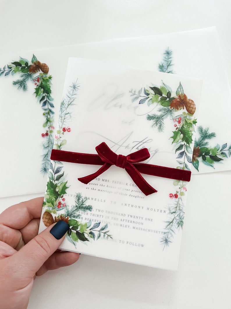 Printed vellum jacket with pine and holly leaves in the bottom left corner and top right corner. Christmas vellum jacket includes pine cones and is perfect for your Christmas wedding invitation.