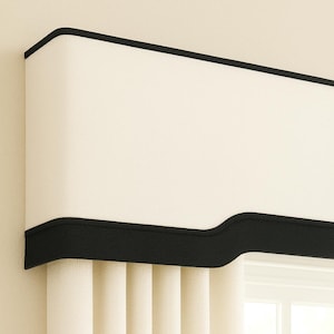 May include: Cream-colored window valance with a black trim. The valance is mounted above vertical blinds, with a window visible in the background. The design is simple and elegant, suitable for various interior styles.