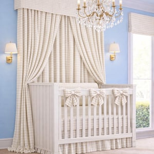 May include: A white crib with a gingham patterned skirt and bows, set against a backdrop of matching curtains and a valance. A crystal chandelier hangs above, with wall sconces on a light blue wall.