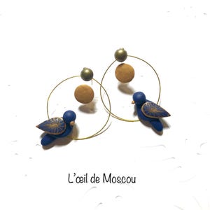 Orecchini di design raffiguranti un uccellino illuminato dalla luna, nei toni del blu notte e dell'oro, modellati a mano, con base in acciaio inossidabile.