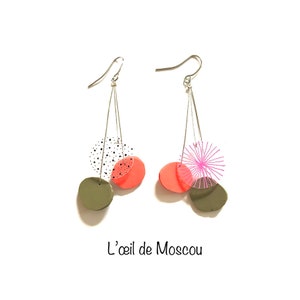 May include: A pair of dangle earrings with silver hooks. Each earring features a combination of olive green, coral, and clear circular shapes. One earring has a black and white polka dot circle, while the other has a pink starburst design. The text "L'oeil de Moscou" is at the bottom.