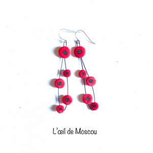 May include: A pair of dangle earrings featuring red poppy flower charms. The earrings are made of silver and have a black wire connecting the charms. The charms are of varying sizes and are arranged in a cascading pattern.