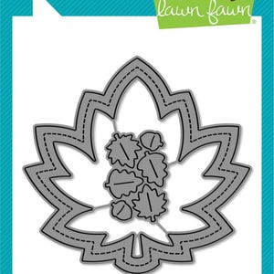 May include: A gray die-cut of a maple leaf with a stitched outline and interior details. The die-cut includes smaller leaf and acorn shapes within the larger leaf frame. The words "lawn cuts" and "custom craft dies" are visible.