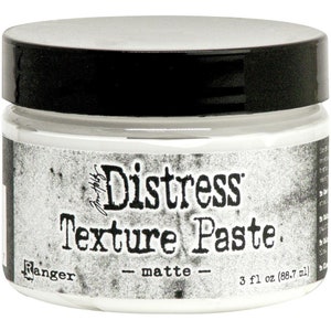 May include: A jar of matte white Distress Texture Paste by Ranger. The jar has a black lid and a label with the product name and brand. The label also indicates the volume is 3 fl oz (88.7 ml).