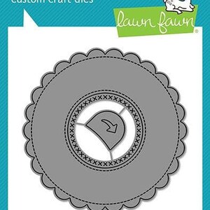 May include: A gray metal die cut for crafting, shaped like a circle with a scalloped edge. The die cut has a smaller circle in the center with a stitched design and a small arrow pointing to the left.