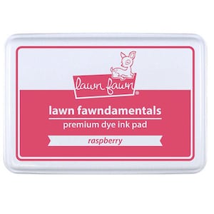 May include: A white ink pad with a pink label. The label says "lawn fawn" with a small deer logo. The label also says "lawn fawnamentals premium dye ink pad" and "raspberry".