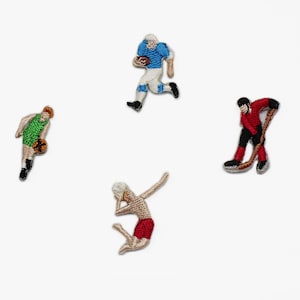 May include: Four embroidered patches depicting sports figures. A football player in blue and white, a basketball player in green, a hockey player in red and black, and a gymnast in red and tan.