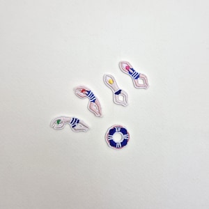 May include: Embroidered patches featuring swimmers in blue and white swimsuits, with colorful caps. A blue and white life preserver patch is also included. These patches are ideal for decorating clothing or accessories.