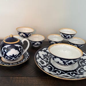 May include: A tea set comprising a small teapot and several bowls with matching saucers. Each item is made of white porcelain, featuring a deep blue floral pattern and finished with a thin gold rim along the edges of the lids, rims, and bases.