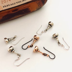 May include: Three pairs of silver and copper earrings with a bottle stopper design. The earrings have a hook closure.