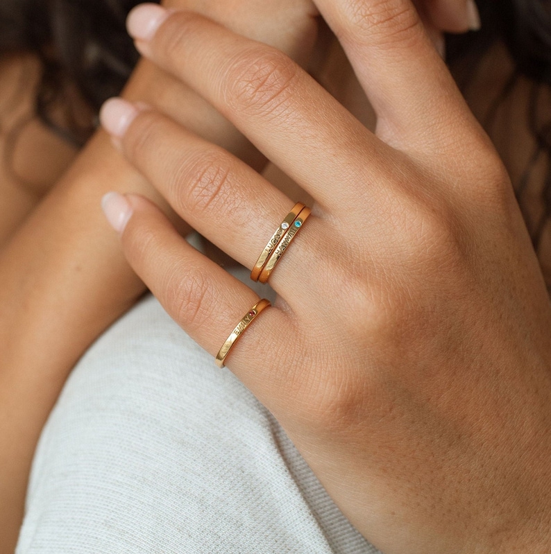 Three gold rings stacked on finger, with blue gemstone and engraved words 'Love' and 'Always'