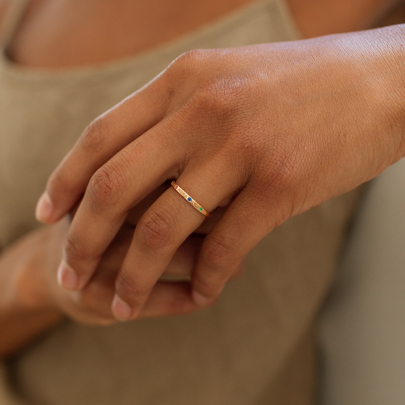A thin gold band ring with three small gemstones. The gemstones are red, green and blue