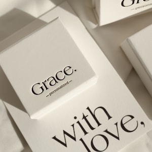 May include: White gift box with the text "Grace. -personalized- " printed on the top. The box is sitting on a white surface with the text "With love." printed on it.