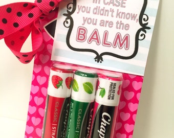 May include: A gift set featuring three ChapStick lip balms in strawberry, spearmint, and a classic flavor. The set is packaged in a pink heart-patterned holder with a pink polka dot bow. The card reads "In case you didn't know, you are the BALM."