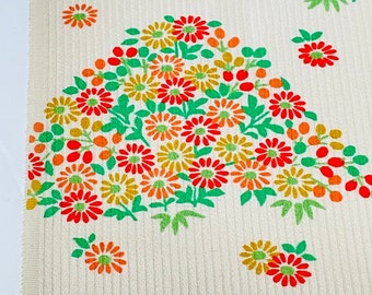 May include: White fabric with a repeating pattern of green leaves and orange, red, and yellow flowers. The flowers are arranged in a cluster and resemble chrysanthemums.