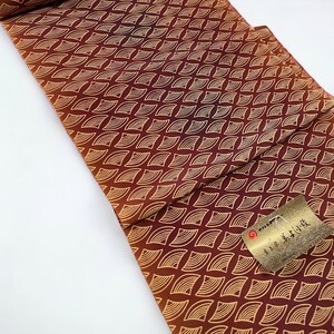 May include: A red and orange fabric with a gold pattern of overlapping crescent shapes. The fabric has a tag with Japanese text that reads "Kyoto Kimono"