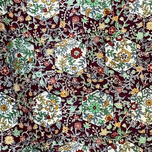 May include: A close-up of a fabric with a repeating pattern of hexagonal shapes filled with a floral design. The fabric is a deep burgundy color with white, green, and yellow flowers.