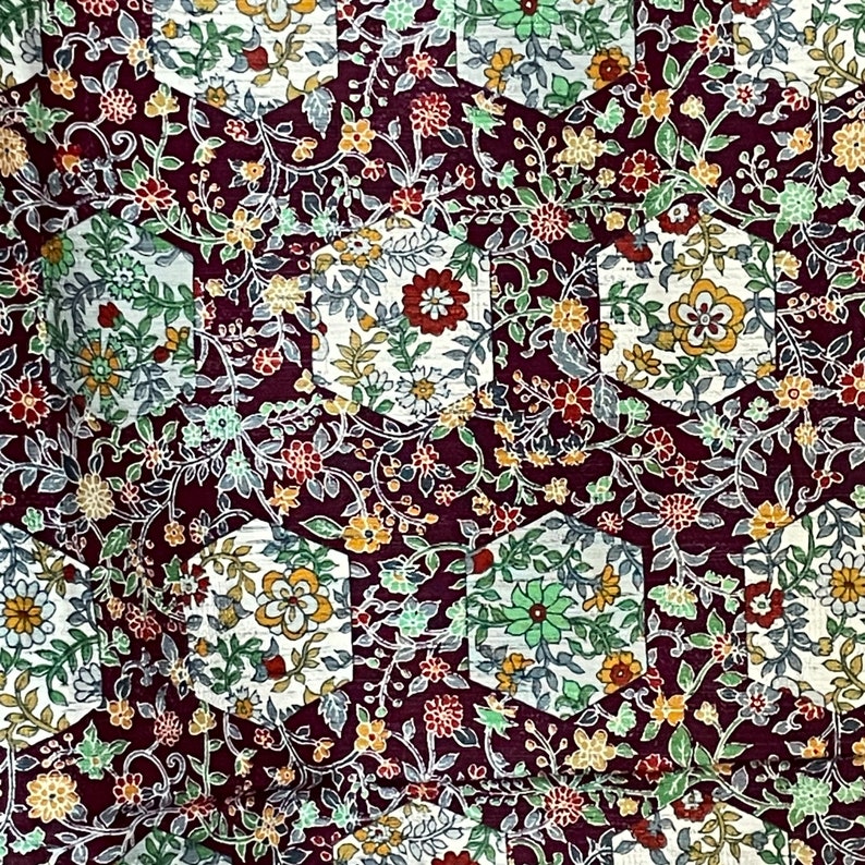 May include: A close-up of a fabric with a repeating pattern of hexagonal shapes filled with a floral design. The fabric is a deep burgundy color with white, green, and yellow flowers.
