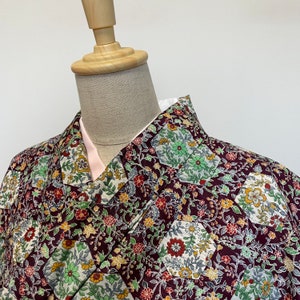 May include: A burgundy kimono with a floral pattern featuring green, white, and yellow accents. The kimono is made of a soft, lightweight fabric and has a traditional Japanese design.